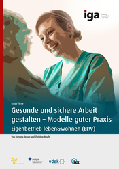 Fotografie einer lächelnden Pflegekraft in grüner Arbeitskleidung, die sich freundlich einem älteren Menschen zuwendet.
