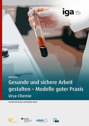 Fotografie einer Hand in weißem Laborkittel, die ein Reagenzglas mit dunkelroter Flüssigkeit hält, vor einem Laborarbeitsplatz. 