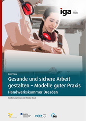 Fotografie zeigt zwei Personen mit roten Gehörschutzkopfhörern, die gemeinsam auf ein Holzprofil blicken.