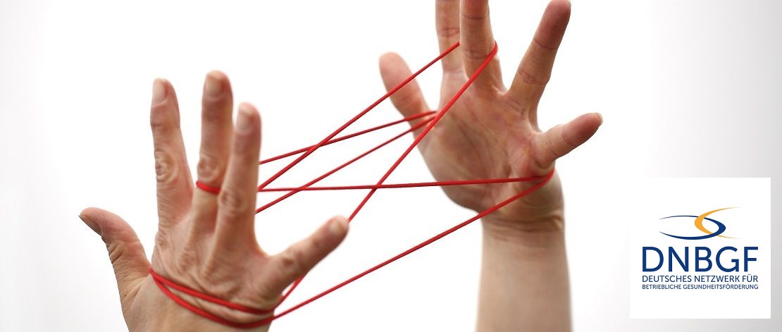 Eine Person hat einen roten Faden um die Finger beider Hände gewickelt. Der rote Faden zeigt die Startposition eines als Fadenspiels.