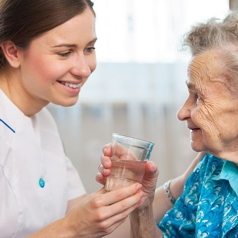Eine junge Altenpflegerin reicht einer Seniorin ein Glas Wasser.