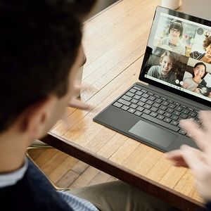 Ein Mann sitzt in einem Café und führt eine Videokonferenz durch. Auf dem Bildschirm sieht man 4 Videokonferenz-Teilnehmer.